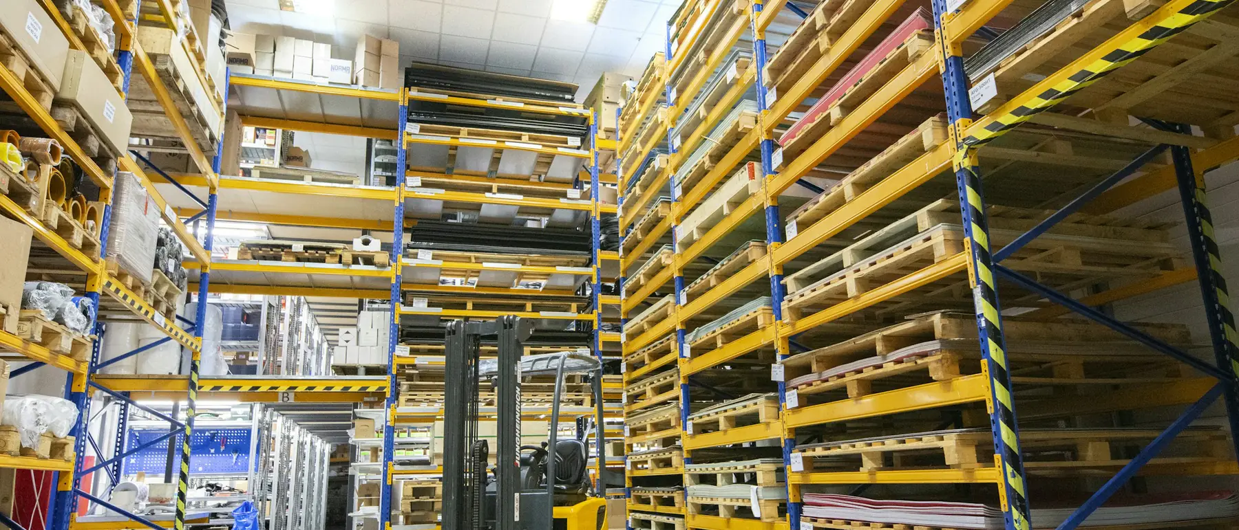 Warehouse racking stacked with palletised goods and a forklift